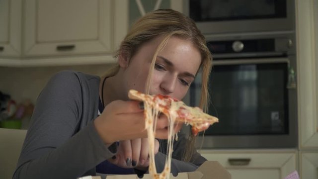 Beautiful blonde eating pizza in the kitchen