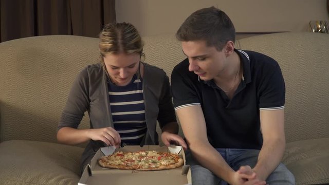 Young couple with a box of pizza sits on the couch