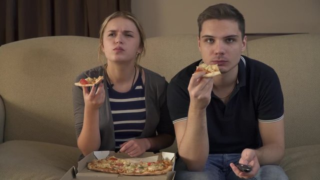 Beautiful young couple sitting on the couch and eating pizza