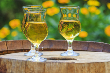 glasses with cider stand on a barrel with yellow flowers in the background