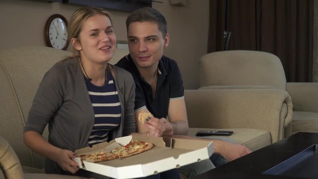 Beautiful young couple sitting on the couch and eating pizza