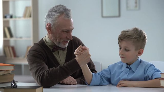 Grandpa winning in arm wrestling with grandson, proud of kid, family leisure