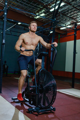Fototapeta na wymiar Fit young man using exercise bike at the gym. Fitness male using air bike for cardio workout at cross training gym.