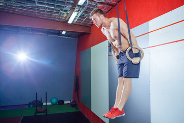 Muscle-up exercise young man doing intense cross fit workout at the gym on gymnastic rings.