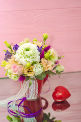 Spring flowers bouquet with decorative heart on pink wood background.