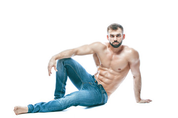 bodybuilder posing. Beautiful sporty guy male power. Fitness muscled in blue jeans. on isolated white background. sits on the floor