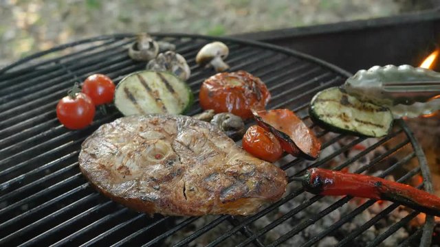 Healthy fish cuisine: grilled steaks from white sea fish with grilled vegetables, chili pepper, rosemary sprig, zucchini, cherry tomatoes and mushrooms, cooking process, the chef turns the grill