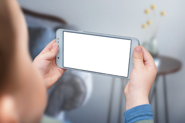 Boy holding smartphone in horizontal position with empty white screen. Kid play game, surfing online, learning...etc. Mockup