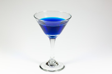 Halloween inspired blue color cocktail in a clear glass sitting on a white table waiting to be enjoyed.