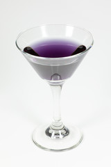 Halloween inspired purple color cocktail in a clear glass sitting on a white table waiting to be enjoyed.
