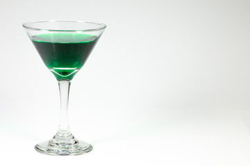 Halloween inspired green color cocktail in a clear glass sitting on a white table waiting to be enjoyed.