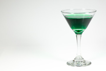 Halloween inspired green color cocktail in a clear glass sitting on a white table waiting to be enjoyed.