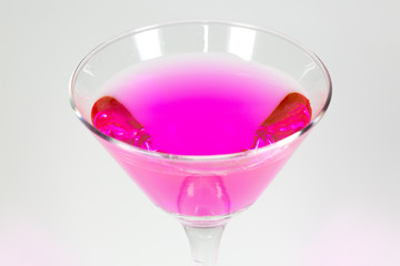 Halloween inspired Pink color cocktail in a clear glass sitting on a white table waiting to be enjoyed.