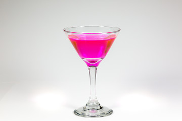 Halloween inspired Pink color cocktail in a clear glass sitting on a white table waiting to be enjoyed.