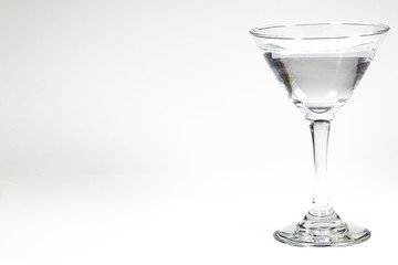 Halloween inspired clear color cocktail in a clear glass sitting on a white table waiting to be enjoyed.