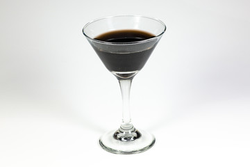 Halloween inspired black color cocktail in a clear glass sitting on a white table waiting to be enjoyed.