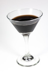 Halloween inspired black color cocktail in a clear glass sitting on a white table waiting to be enjoyed.