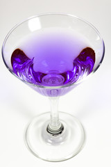 Halloween inspired purple color cocktail in a clear glass sitting on a white table waiting to be enjoyed.