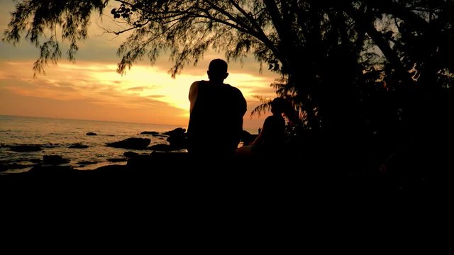 Liebespaar sitzt auf Felsen am Ozean und beobachtet Sonnenuntergang