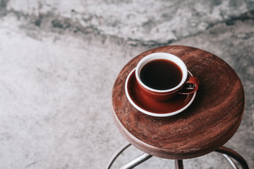 Black filter coffee on a dark brown plate from above. Wooden table, gray concrete floor,  hipster coffee shop. Copy space 
