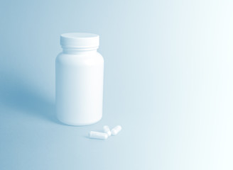 White bottle with pills, three white capsules next to it. Concept: drugs, medicines, placebo