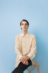 Handsome young thin dark-haired guy with blue eyes wearing yellow shirt posing over blue wall