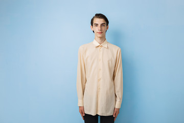 Fototapeta premium Handsome young thin dark-haired guy with blue eyes wearing yellow shirt posing over blue wall