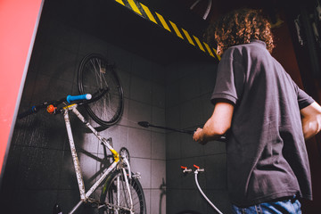 Services professional washing of a bicycle in the workshop. Close-up of hand Young Caucasian stylish man doing bicycle cleaning using automatic electric water pump. Sprays scatter from the pressure