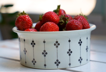 Fresh red strawberries in a white cup on a wooden table on summer afternoon on balcony