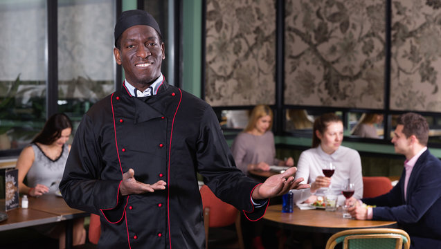 Smiling politely African American chef inviting to visit cozy restaurant