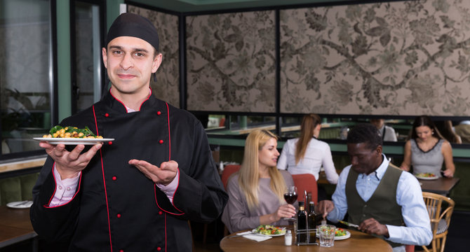 Confident chef with dish in restaurant hall