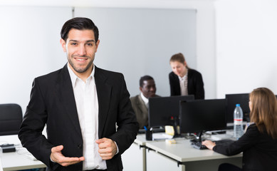 Young businessman standing in office near working colleagues