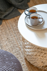 Two mugs of tea on the table-basket with a knitted plaid inside. Modern interior of the room.