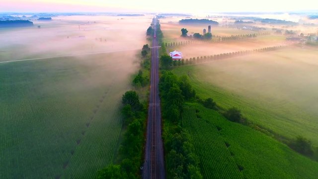 Freight train rolls across foggy rural landscape at sunrise with ethereal beauty, aerial view.