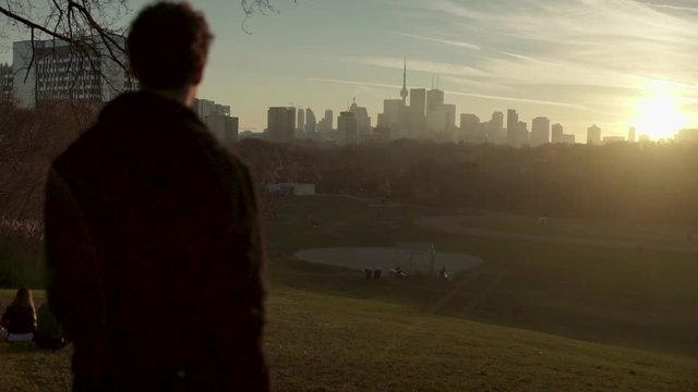 Beautiful Skyline of Toronto at Sunset with Silhouette of a Young Mixed Race Man in the Foreground, Slow Motion Steadicam Push In and Contrast Between Urban City and Green Park, Slow Motion