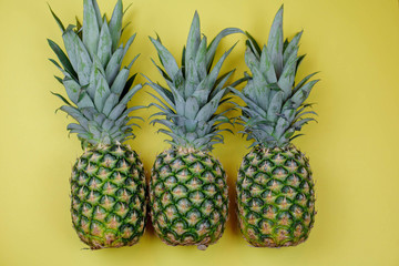 Three whole pineapples in a row on yellow background - fresh healthy eating concept