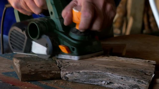 Wood worker using an electric planer on a small piece of wood, a cross section of an old log.