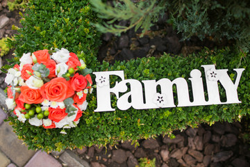 a wedding bouquet lies on the lawn, next to a wooden plaque with an inscription family