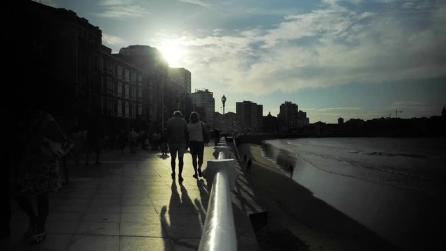 4 k seaside while the sunset with walking people, dramatic clouds on a blue sky, ocean waves and city buildings