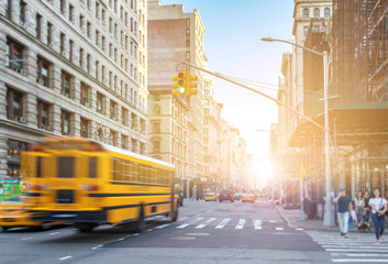 Yellow bus driving fast down Fifth Avenue in Manhattan New York City with sunlight shining in...