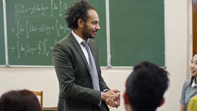 Handheld medium shot of middle eastern man with curly hair explaining equations to multi ethnic group of students after lecture