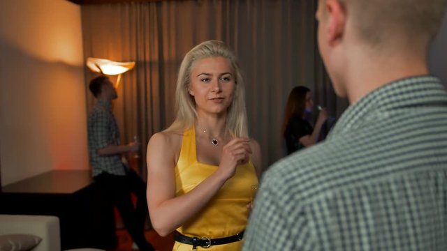Sexy Young lady and guy flirting in flat apartment party, drinking sparkling champagne. Hints at the continuation of the evening in an intimate atmosphere. Other birthday guests at bg. Slow motion