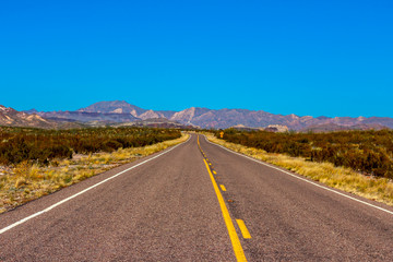 Fototapeta na wymiar Long empty road leading into the mountains with a bright blue sky 