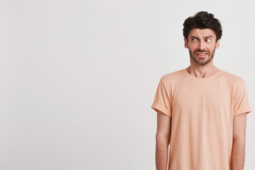 Closeup of scared fearful young man with bristle wears peach t shirt feels frightened and looks to the side isolated over white background