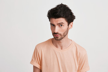 Closeup of serious handsome young man with bristle wears peach t shirt feels confident and looks...