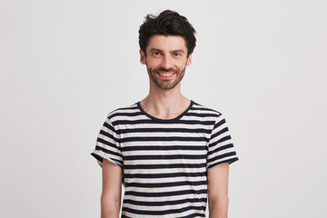 Obraz premium Closeup of cheerful handsome young man with bristle wears striped t shirt feels happy and looks directly in camera isolated over white background
