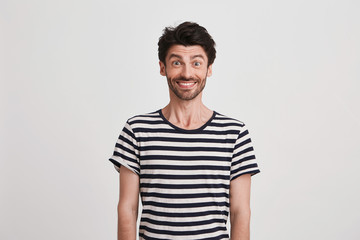 Portrait of happy attractive young man with bristle wears striped t shirt feels excited and smiling...