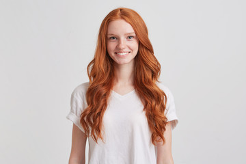 Portrait of cheerful beautiful young woman with long wavy red hair and freckles looks happy and...