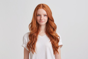Closeup of happy attractive young woman with long wavy red hair and freckles wears stylish t shirt looks happy and smiling isolated over white background - Powered by Adobe