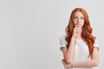 Closeup of cute thoughtful redhead young woman with long wavy hair and freckles wears stylish t shirt thibnking and planning her working day isolated over white background - Powered by Adobe